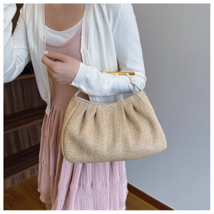 Close-up of woven straw bag with golden cylinder handle and white twisted rope detail