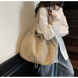 Detail view of a large beige nylon tote bag with drawstring closure and dual front pockets