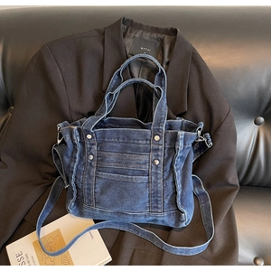 Detail shot of navy denim tote bag with metal rivets and shoulder strap on a black blazer