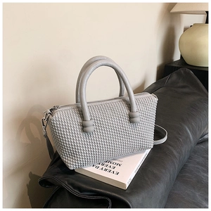 Detail of grey quilted handbag showing square embossed texture and spherical handle accents