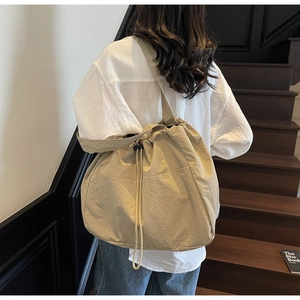 Detail view of the drawstring closure and pleated nylon texture on a beige tote bag