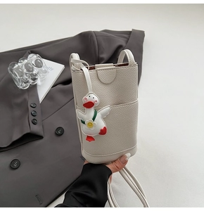 Détail de la mini pochette bandoulière crème avec texture grainée et charm canard mignon
