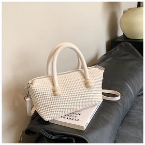Detail of cream woven textured handbag with cylindrical handles and metal zipper closure