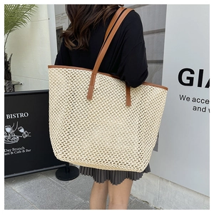 Side view of a large straw woven tote bag with brown straps worn by a model in the street