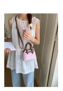 Detail of pink woven shell bag with brown leather handles and adjustable shoulder strap