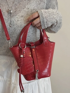 Red crocodile pattern bucket bag with top handle and shoulder strap worn by model