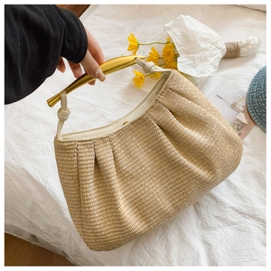 Close-up of woven straw shoulder bag featuring pleated texture and gold crescent handle