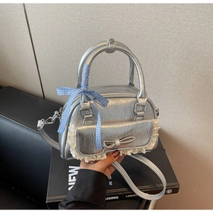 Detail der silbernen Faltenhandtasche mit weißem Spitzenbesatz und blau kariertem Band