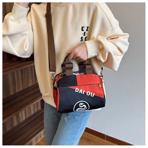 Détail du sac bandoulière rouge et noir avec lettrage DAI OU et sangle en nylon réglable