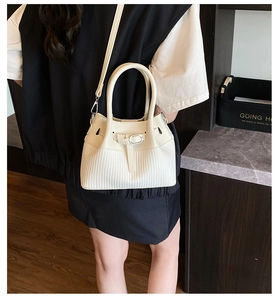 Detail of off-white bucket bag featuring leather stitching and woven texture on model