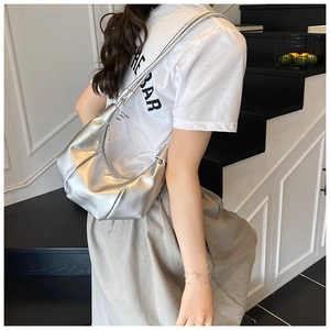 Detail view of silver pleated dumpling bag with leather strap on model in indoor setting