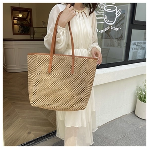 Detail of hand-woven straw tote bag featuring brown leather handles and airy texture