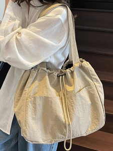 Large beige nylon drawstring tote bag worn over the shoulder for casual travel and daily use