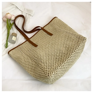 Close-up detail of the woven straw tote bag with brown leather handles on a white fabric