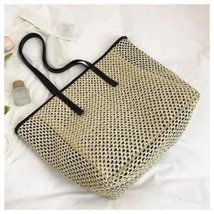 Detail of hand-woven straw tote bag featuring black leather handles on a white background