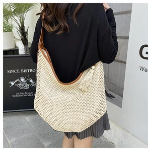 Close-up of woven straw shoulder bag featuring brown leather straps and a stylish side tassel