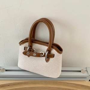 Detail of woven canvas texture and brown leather trim on a stylish shell handbag