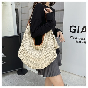 Detail of a large straw shoulder bag with leather handles and decorative fringe tassel