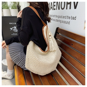 Detail of a large woven straw tote bag with brown leather straps and decorative tassel