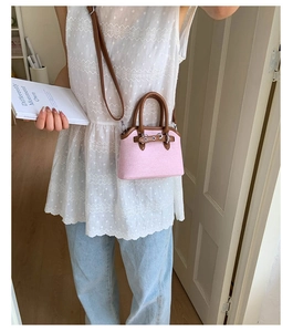 Detail view of pink woven shell bag with brown leather handles and silver buckle hardware
