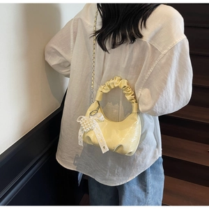 Detail of yellow patent leather hobo bag with pearl heart charm and lace bow
