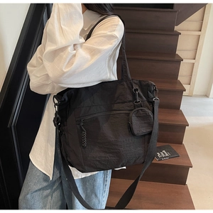 Detail of black nylon tote bag featuring a large front zipper pocket and a mini coin purse