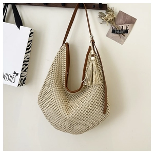 Detail of a beige woven straw tote bag featuring brown leather straps and tassel charm