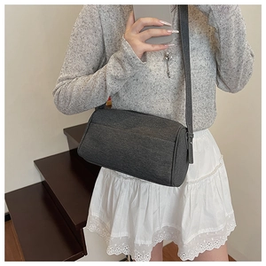Close-up of a dark grey cylinder crossbody bag with canvas texture on a female model