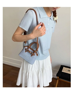 Close-up of a blue fabric shell bag with brown leather handles and a long shoulder strap