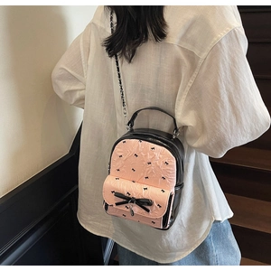 Pink seersucker backpack with black bow prints and metal chain strap shown on a model