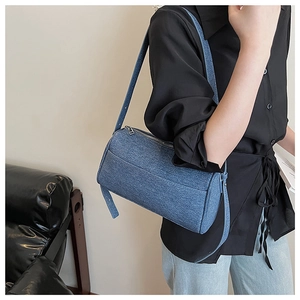 Close-up of a dark blue denim cylinder shoulder bag featuring textured fabric and silver zipper