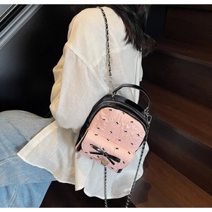 Detail view of mini backpack featuring pink bow pattern and metallic chain strap worn by model