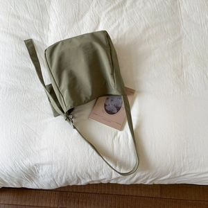 Dettaglio di una borsa tote in tela verde scuro su un fondo in tessuto bianco
