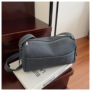 Detailed texture of dark grey pillow bag with metal zipper on a white book prop