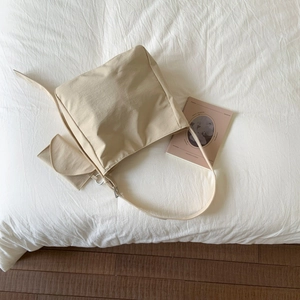 Vista dall'alto di una borsa tote in tela beige con tasca laterale su letto bianco