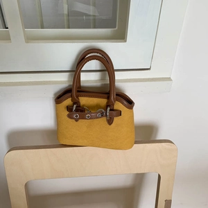Close-up of mustard shell bag with brown leather trim on a modern wooden chair