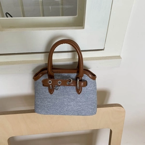 Close-up of the light blue textured fabric and brown leather trim on the shell-shaped handbag