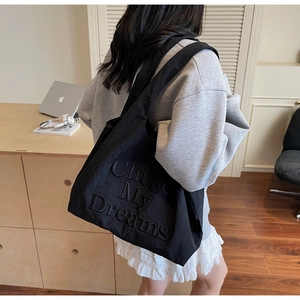 Détail du sac cabas en toile noire avec broderie porté par un mannequin en intérieur