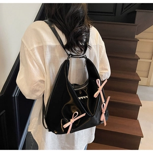 Dettaglio della borsa hobo nera lucida con fiocchi rosa indossata sulla spalla