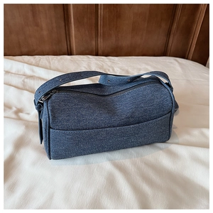 Detail of blue denim cylindrical shoulder bag with metal zipper and adjustable strap