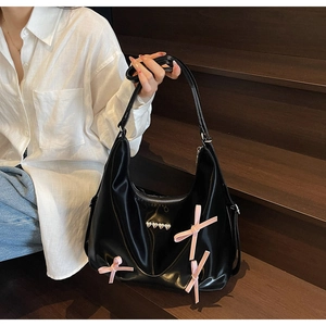 Dettaglio borsa a mezzaluna nera lucida con fiocchi rosa e rivetti a cuore argento su camicia