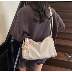 Detail view of cream canvas crossbody bag with pink heart charm and braided straps