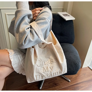 Détail de la broderie 'Chase My Dreams' sur un sac cabas en toile crème avec bouton pression