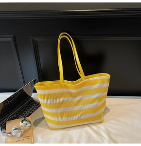 Detail of woven tote bag featuring yellow and cream stripes with slim leather shoulder straps