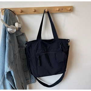 Detail view of black nylon tote bag with front zipper pocket and mini coin pouch accessory