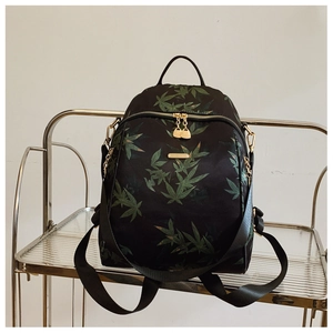 Détail du sac à dos noir avec motif de feuilles d'érable vertes et fermetures éclair dorées