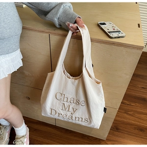 Détail de la broderie 'Chase My Dreams' sur un sac cabas en toile crème avec large bandoulière