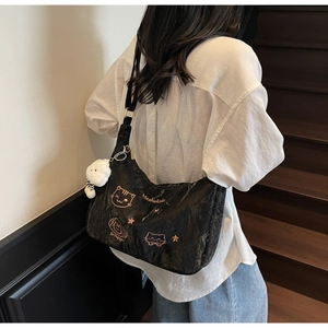Close-up of black crossbody bag with cat embroidery and plush pendant on model