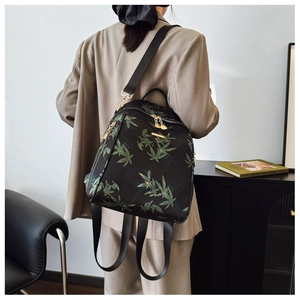 Détails du motif de feuilles vertes et des ferrures dorées sur le sac à dos noir