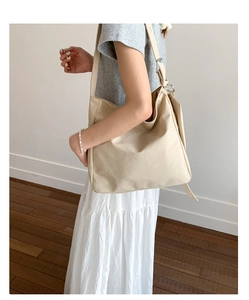 Detail view of a beige canvas tote bag with adjustable strap on a female model